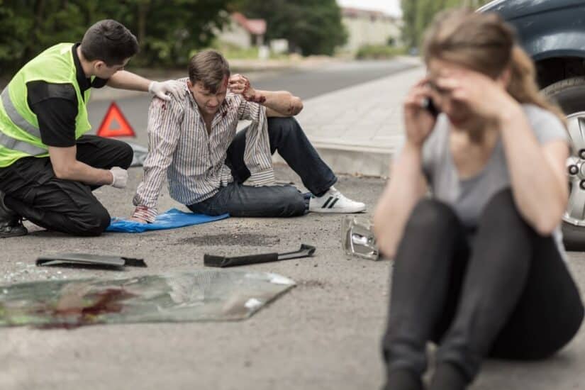 Car Crash Man Sitting On The Ground And A Woman Calling On The Phone Next To A Car Crash Scene